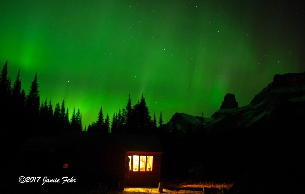 Northern Lights behind cabin in mountains.