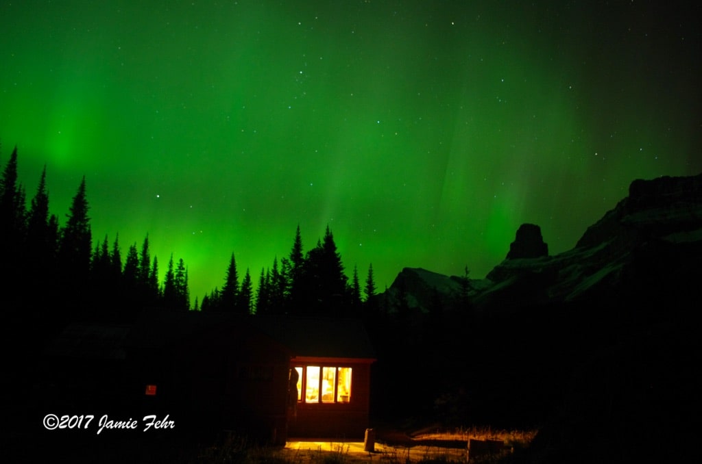 Northern Lights behind cabin in mountains.